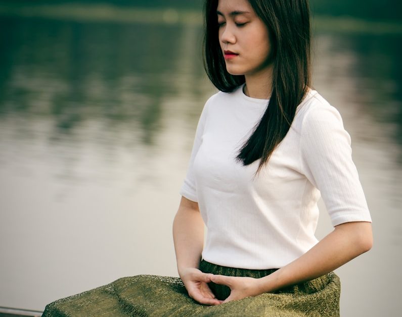 woman meditating on wooden dock during daytime